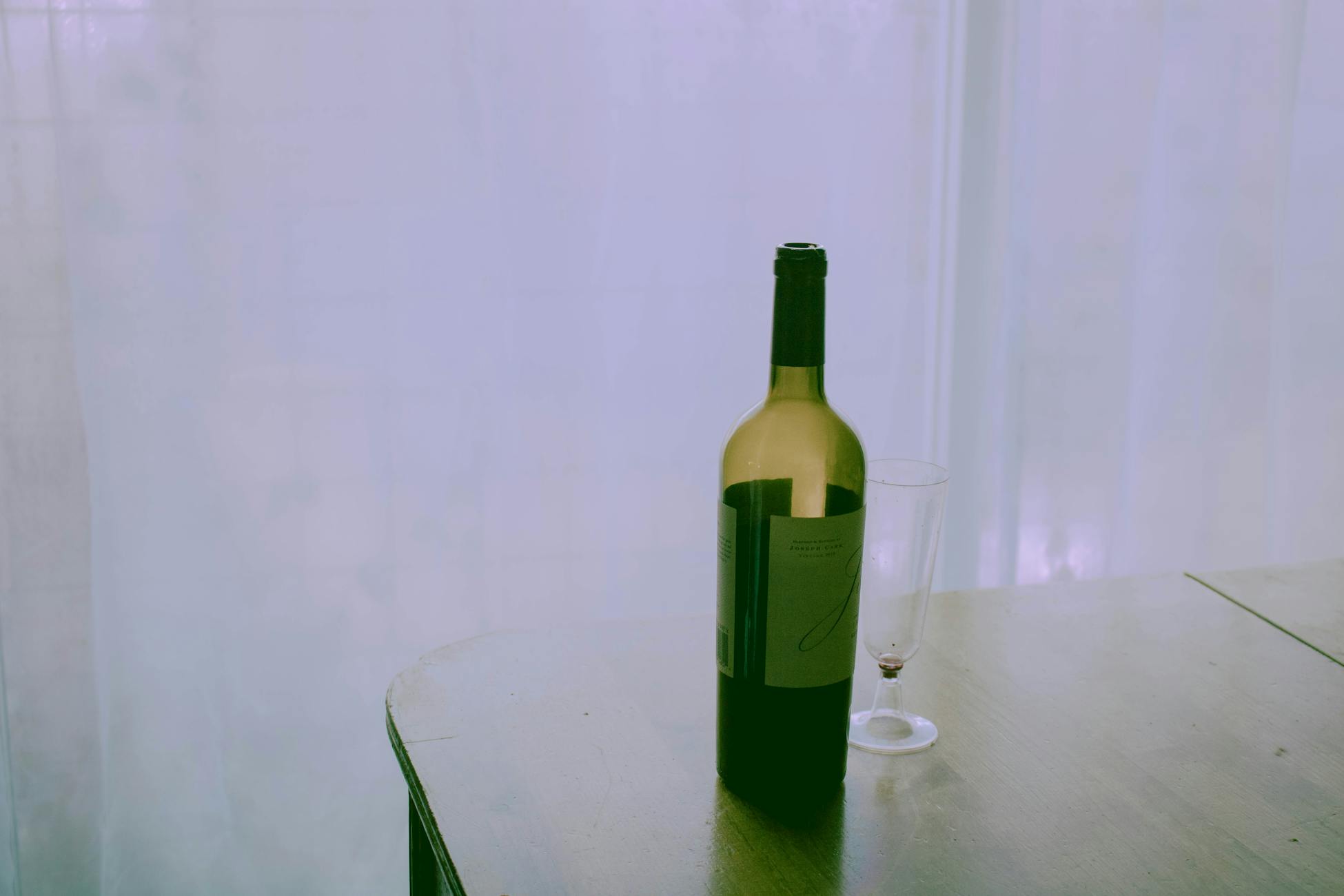 A bottle of wine and an empty glass on a wooden table, minimal setup.