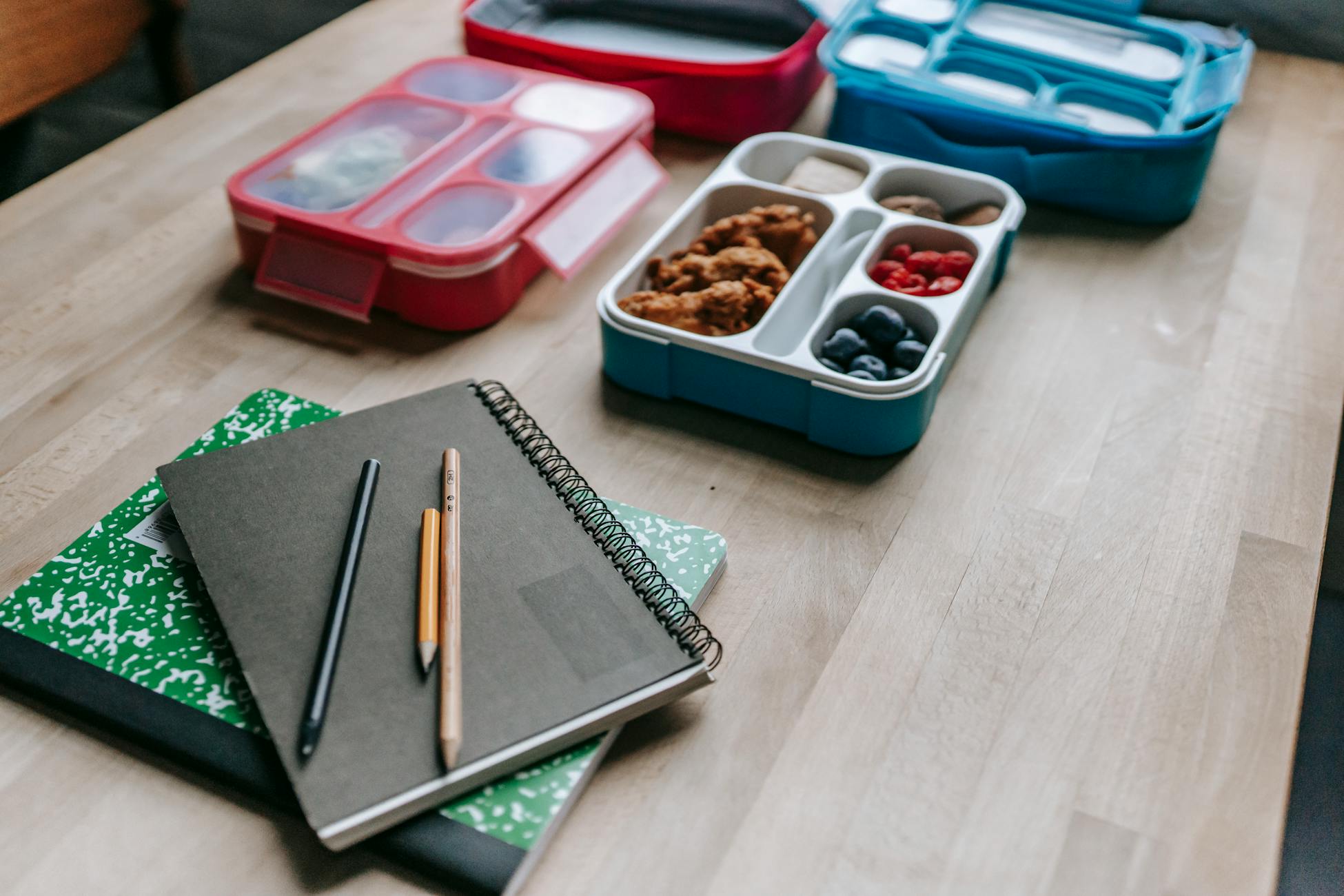 Notebooks with pencils beside healthy lunchboxes on a wooden table, perfect for school or work.