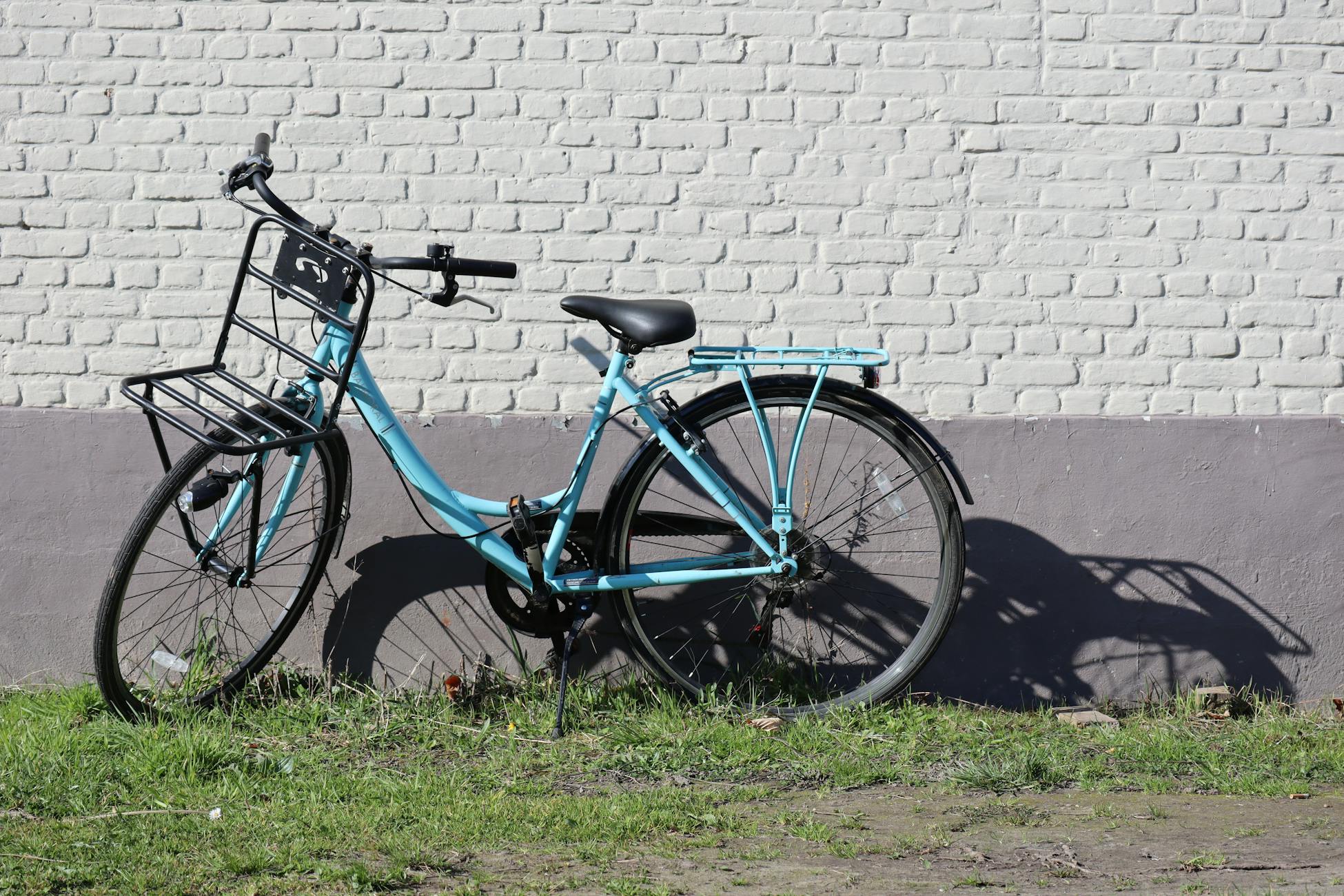 A blue bicycle parked against a white brick wall with green grass in sunlight.