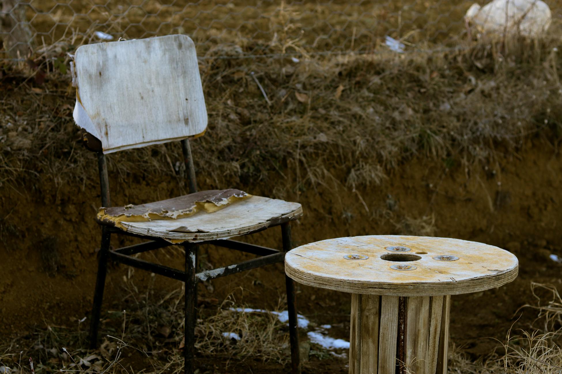 Aged rusty metal chair with white round table on grassy ground in countryside