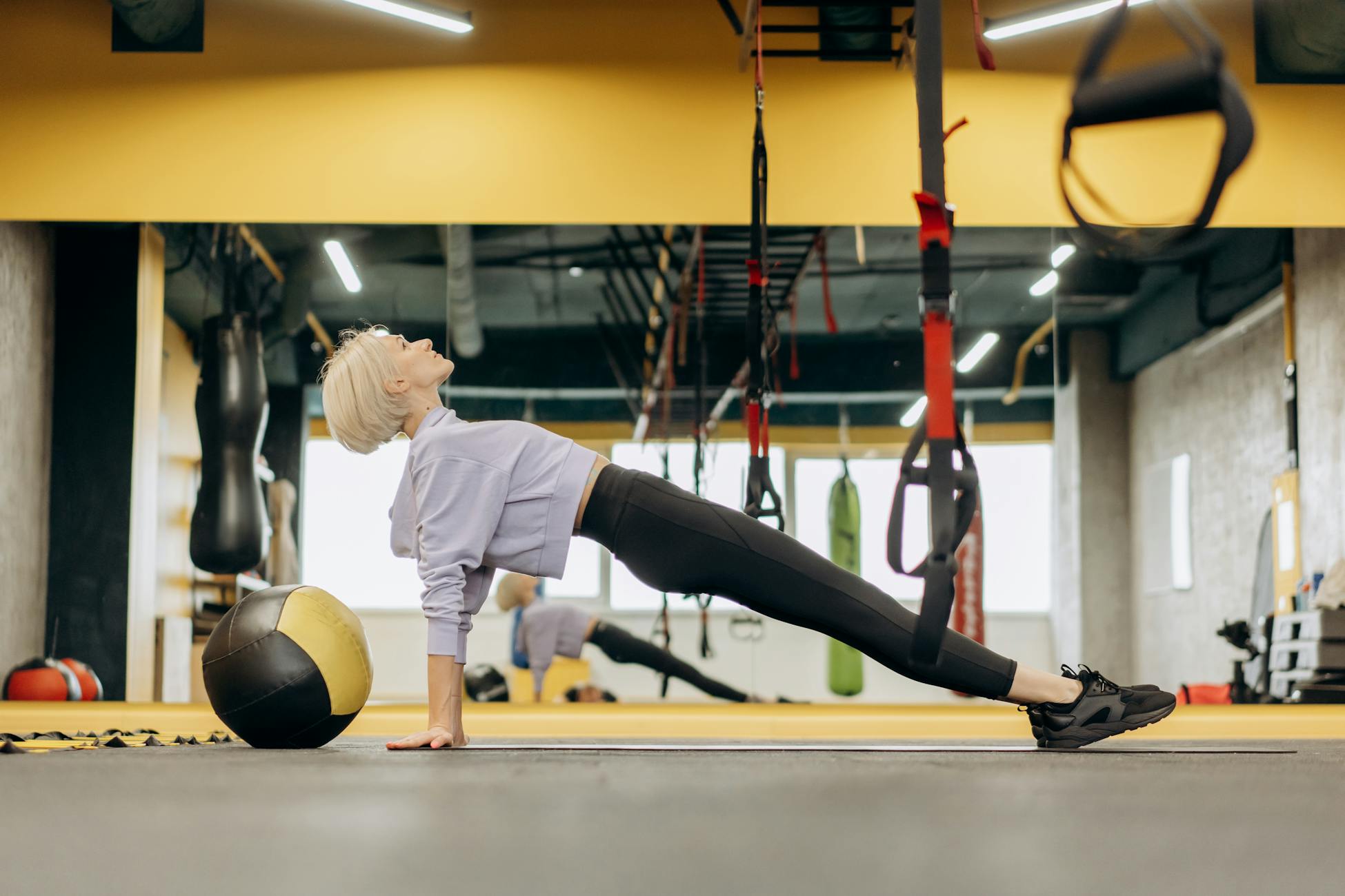 Female athlete practicing Pilates with a medicine ball in a modern gym setting.