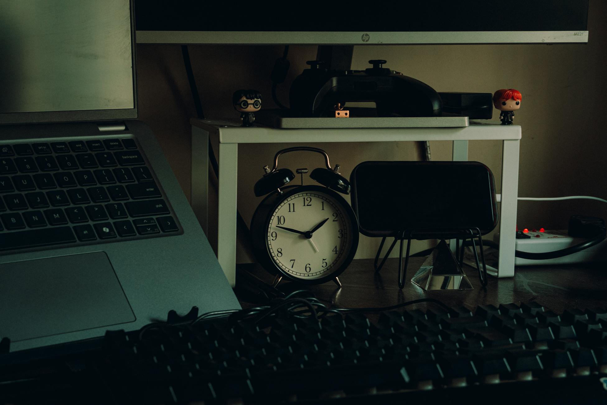 Tidy desk setup with a laptop, analog clock, and desk decor in a modern home workspace setting.