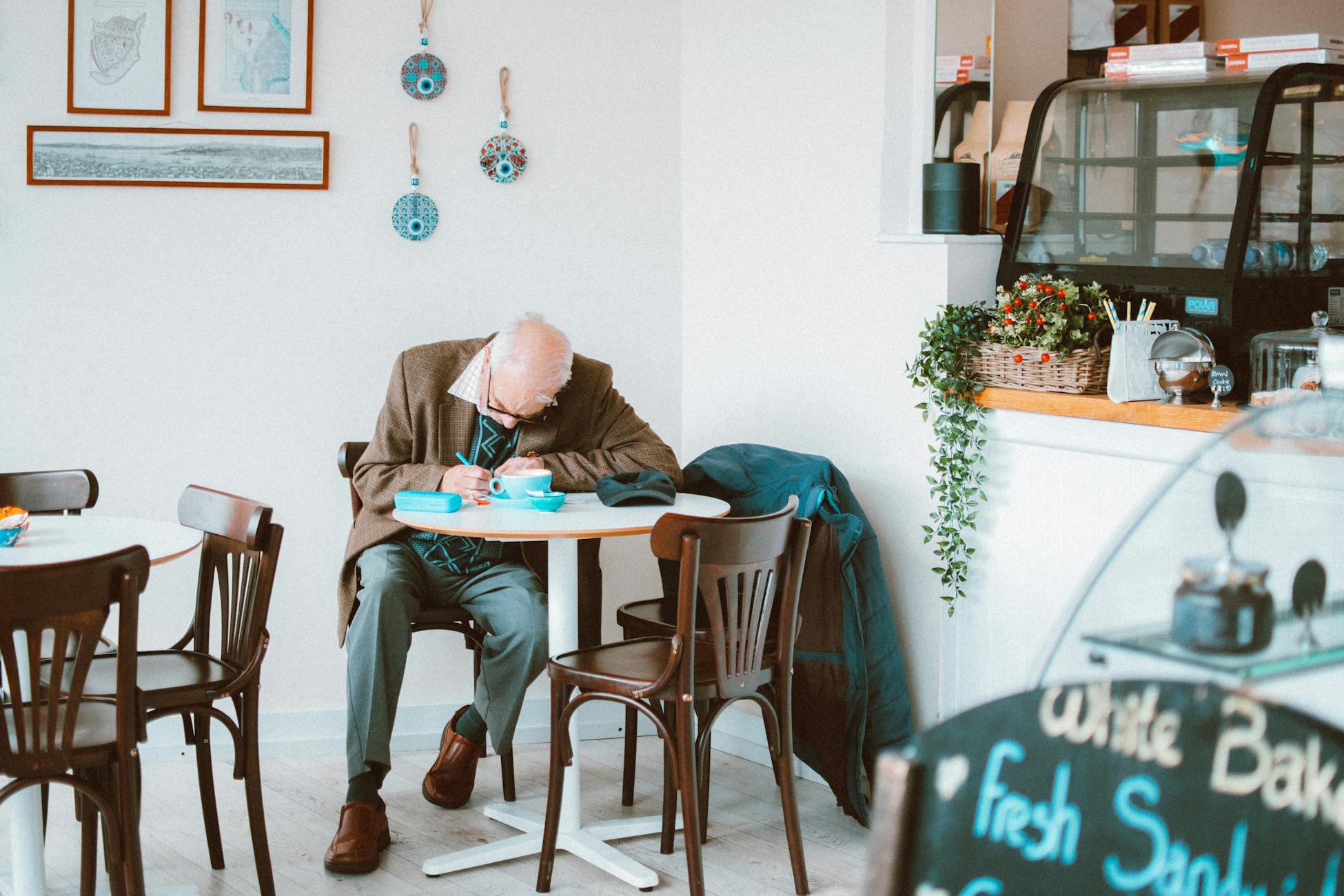 Elderly man writing at a café table, surrounded by cozy decor and ambient lighting.