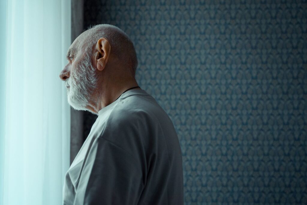 An older man looking thoughtfully out of a sunny window.
