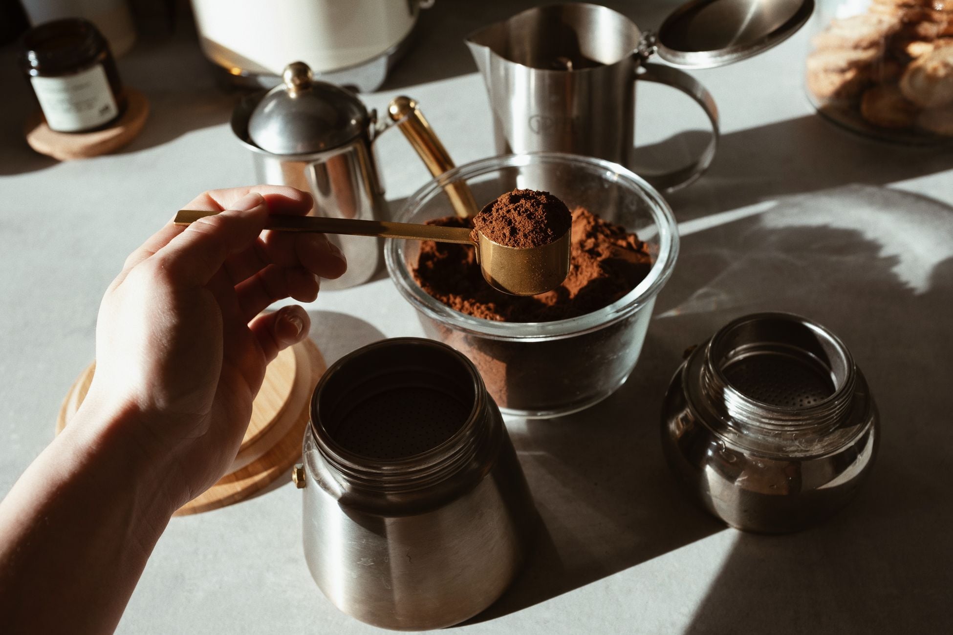 Hand scooping ground coffee from jar with kitchenware setup, ideal for morning brews.