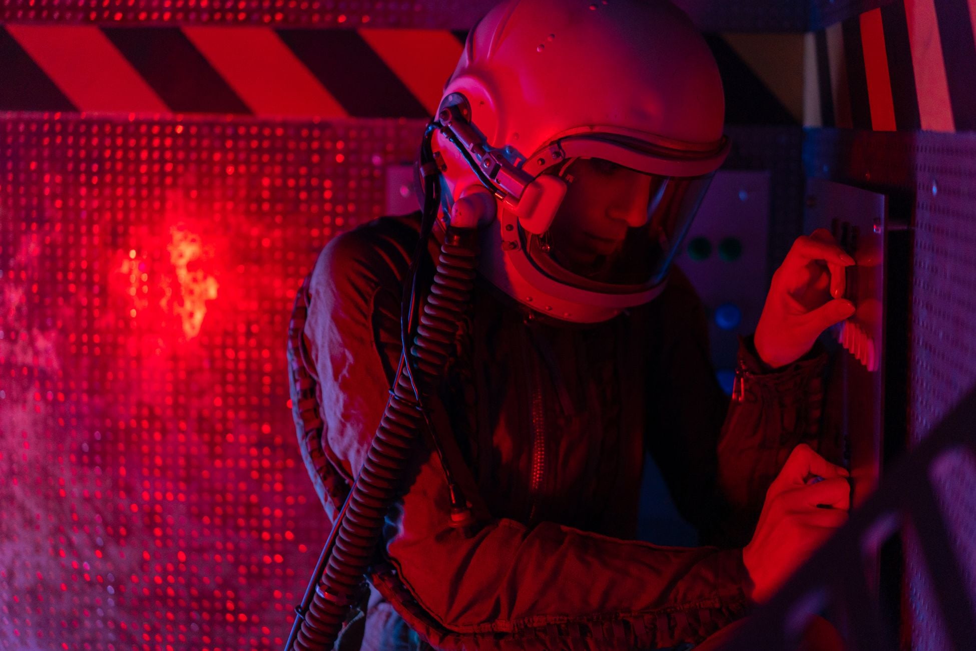 A female astronaut operates a control panel under red lighting, evoking a sci-fi and futuristic atmosphere.