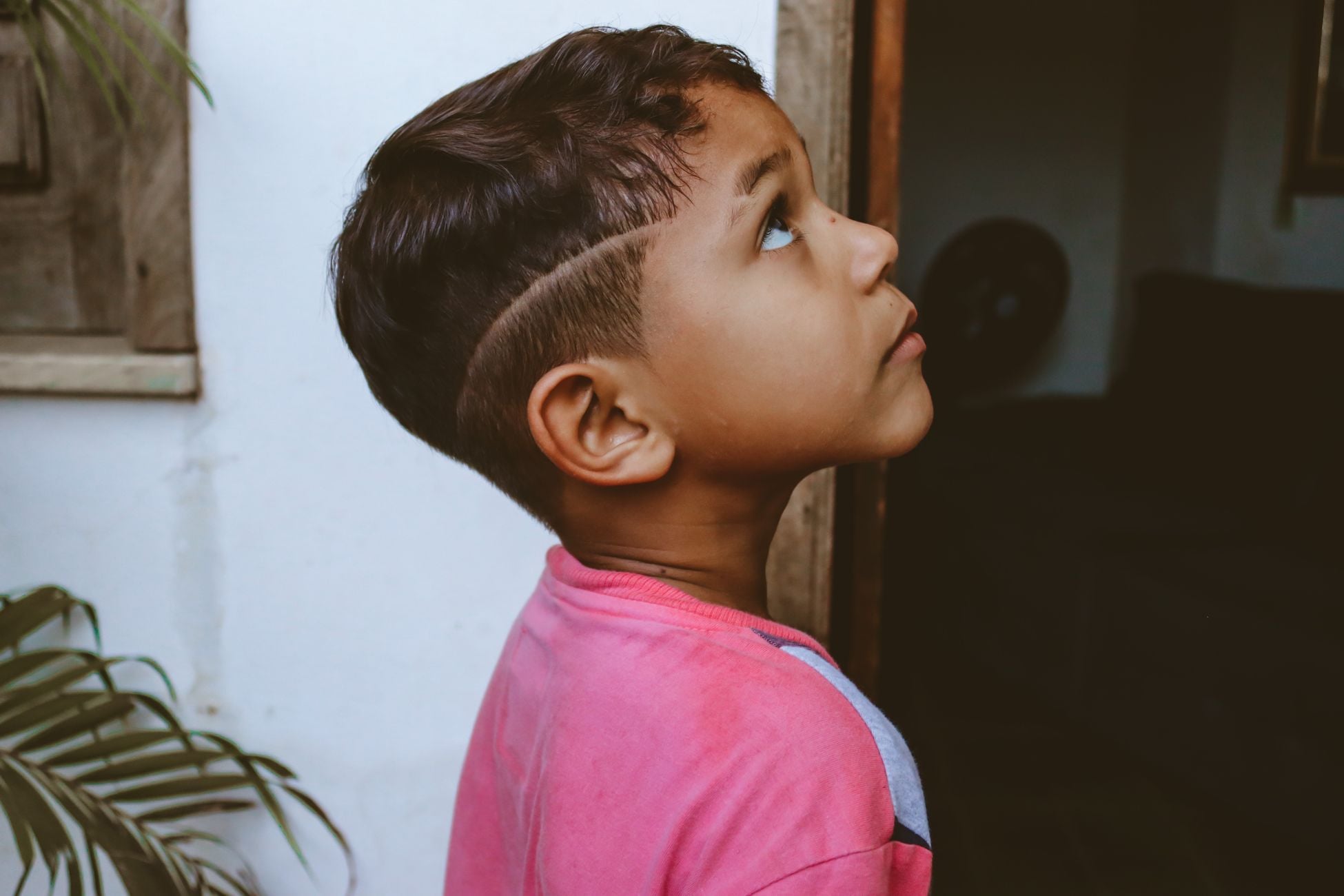 Side profile of a young boy looking upwards with curiosity indoors.