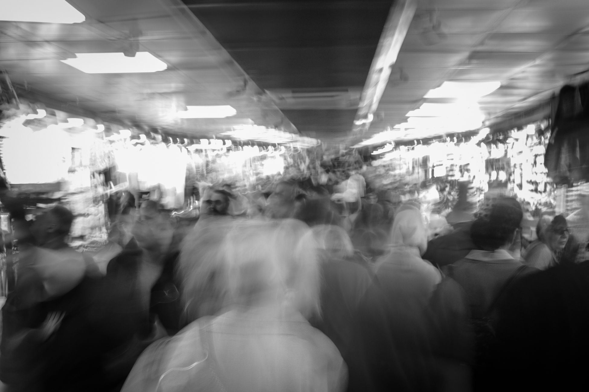 Motion-blurred black and white image of a bustling urban crowd indoors.