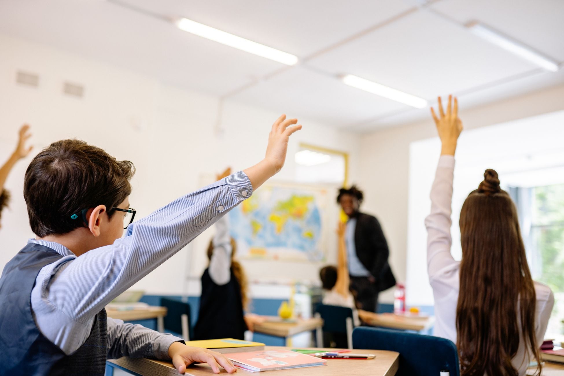 Enthusiastic students participating in a classroom, raising hands to answer teacher's question.