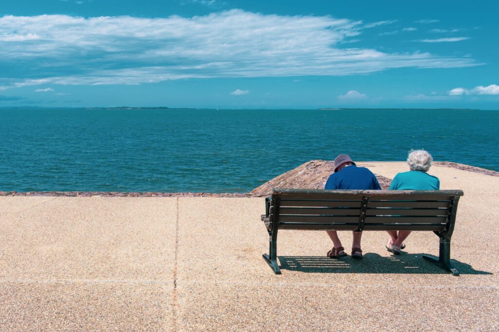 An older couple seated together on a bench overlooking the sea