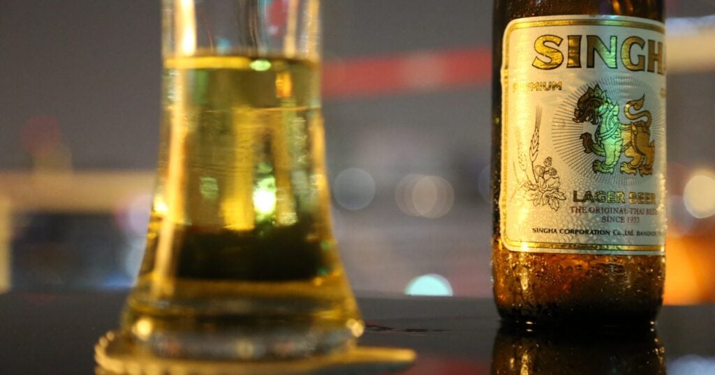 A bottle of Singha lager beer beside a glass at night
