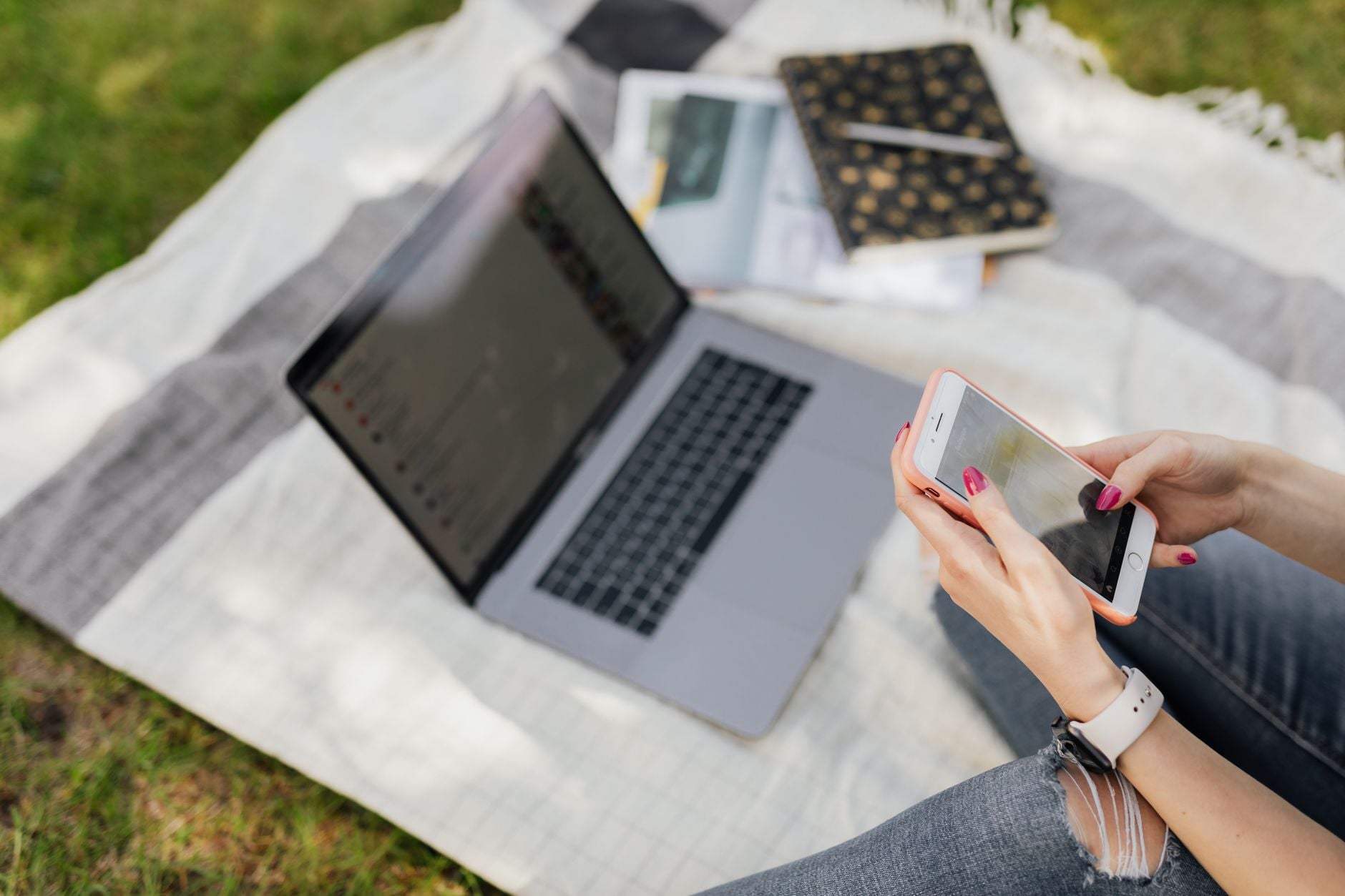 A university student messaging on a phone beside a laptop and notebooks